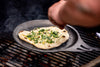 olidteknics Iron Crêpe Pan cooking garlic naan bread on a Big Green Egg grill, highlighting its versatility for flatbreads and high-heat cooking.