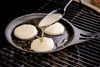 Solidteknics Iron Crêpe Pan being used to cook pancakes on a Big Green Egg grill, demonstrating its versatility and non-stick surface.